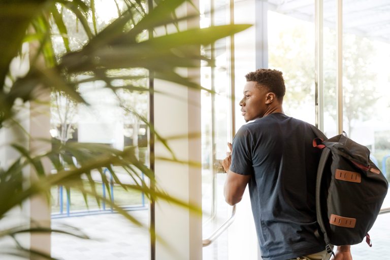 A young man with a backpack on and walking out a door