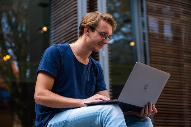 A young man working on his laptop outside and smiling