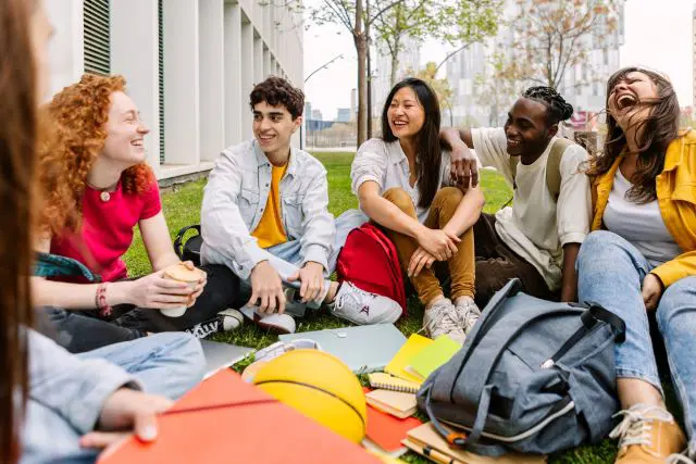 A group of students sitting in the grass on campus and smiling